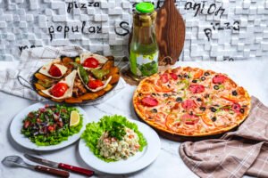 meat sage with salami pizza capital salad vegetable salad and compote on the table